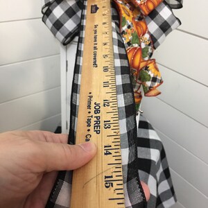 May include: A black and white checkered ribbon with a wooden ruler measuring 16 inches. The ribbon is being measured for a craft project.
