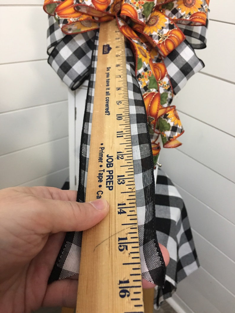 May include: A black and white checkered ribbon with a wooden ruler measuring 16 inches. The ribbon is being measured for a craft project.