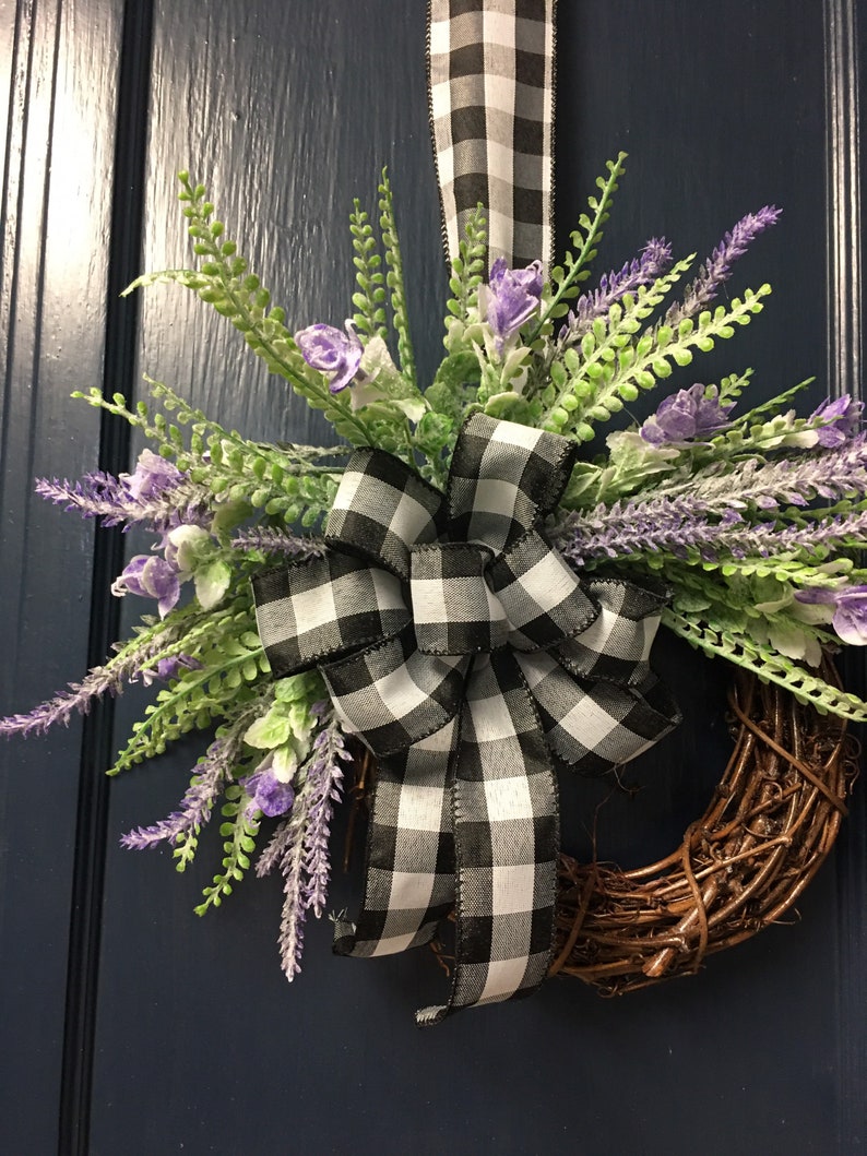 May include: A wreath made of brown twigs with a black and white checkered ribbon bow and purple lavender flowers.