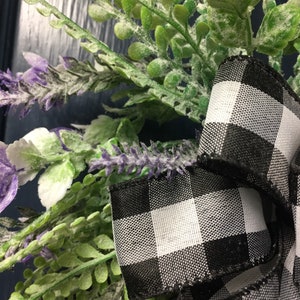 May include: A black and white checkered ribbon tied around a wreath of green leaves and purple flowers.