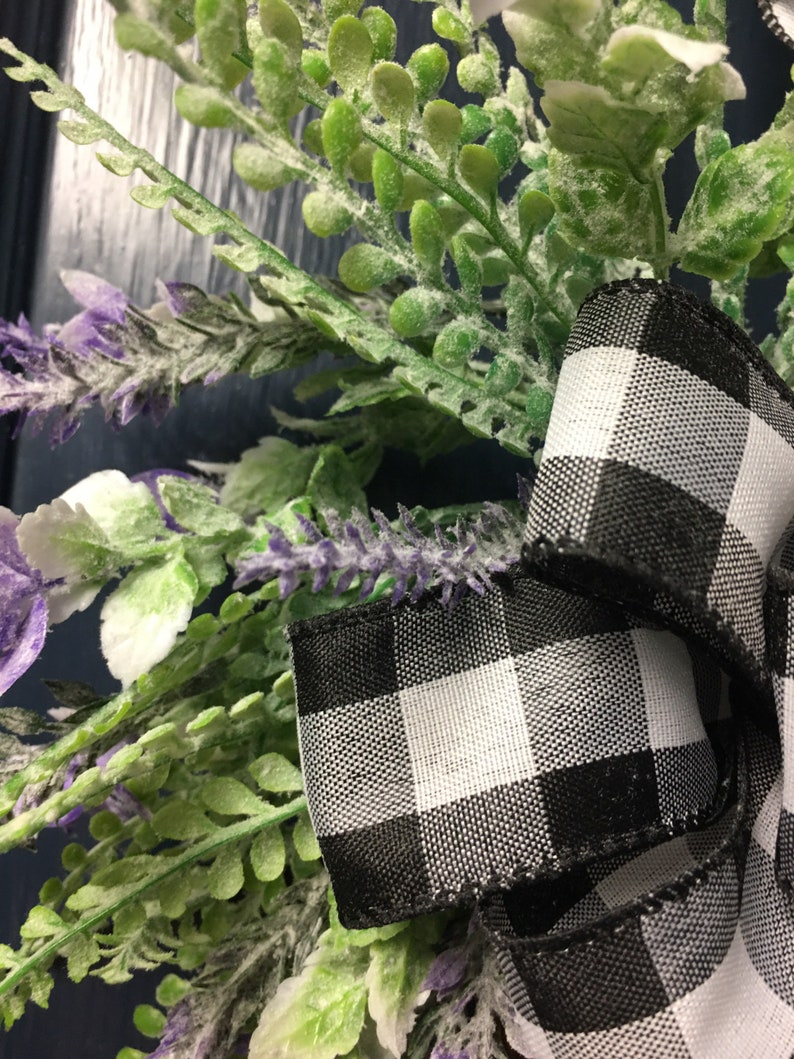 May include: A black and white checkered ribbon tied around a wreath of green leaves and purple flowers.