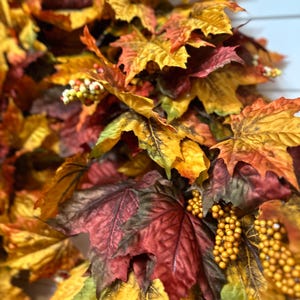 May include: Close-up of a fall-themed garland with maple leaves in shades of red, orange, and yellow. The garland also features small, round, yellow berries. The leaves have detailed veining and a realistic appearance.