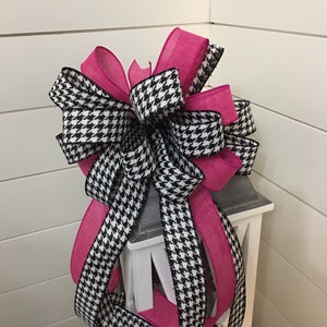 May include: A large, black and white houndstooth ribbon bow with a pink ribbon accent. The bow is tied around a white lantern.