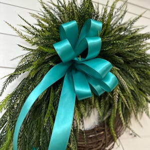 May include: A decorative wreath featuring a teal satin bow and lush green foliage. The wreath is made of woven brown branches, creating a natural and inviting aesthetic. Perfect for adding a touch of elegance to any home decor.