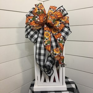 May include: A white lantern with a black and white checkered bow with a pumpkin and sunflower print ribbon. The lantern is sitting on a black and white checkered table cloth.