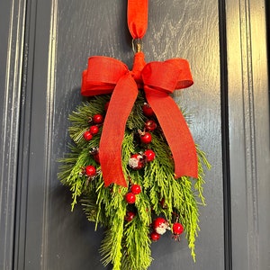 May include: A red and green Christmas swag with a red bow and red berries hanging on a dark blue door.