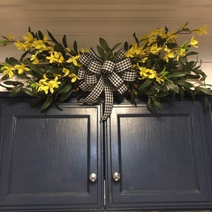 May include: A black and white checkered bow with yellow flowers and green leaves hanging above a dark blue cabinet.