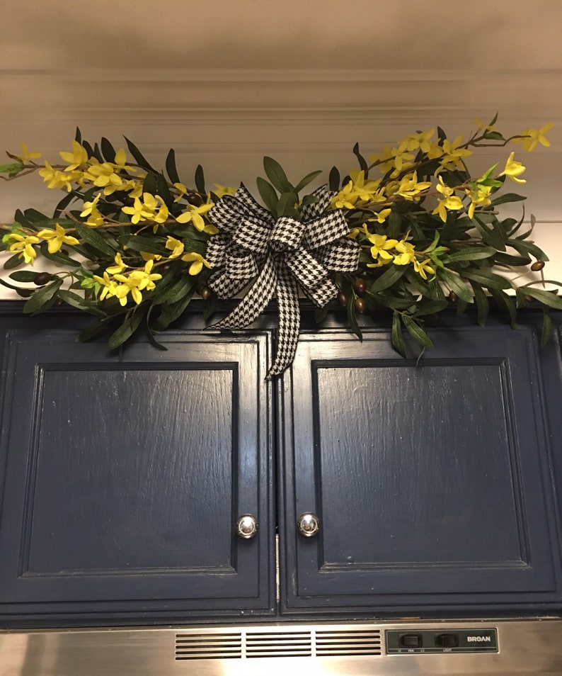 May include: A black and white checkered bow with yellow flowers and green leaves hanging above a dark blue cabinet.