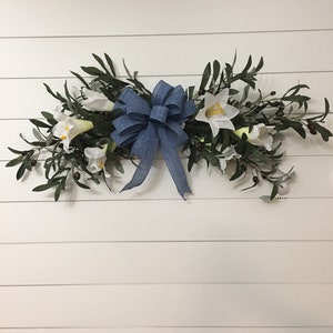 May include: A blue bow with white flowers and green leaves on a white wood background.
