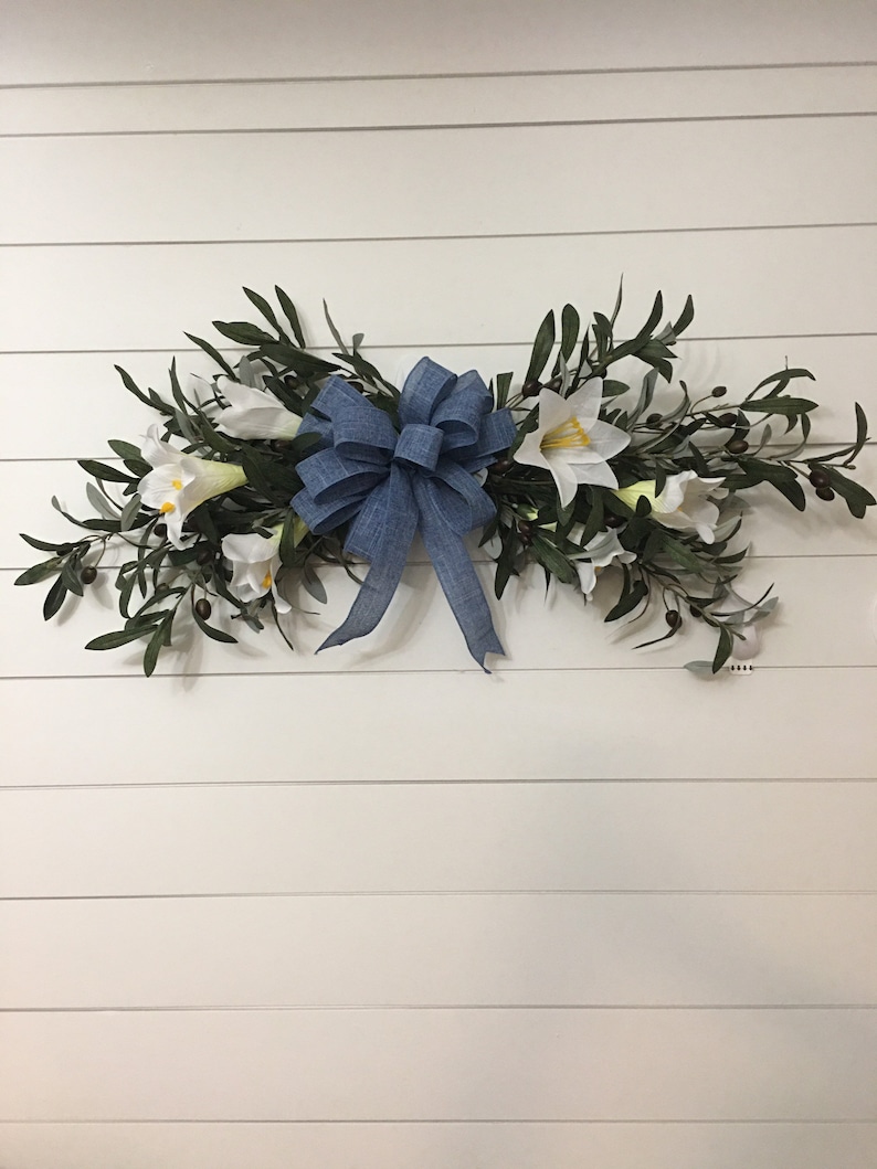 May include: A blue bow with white flowers and green leaves on a white wood background.