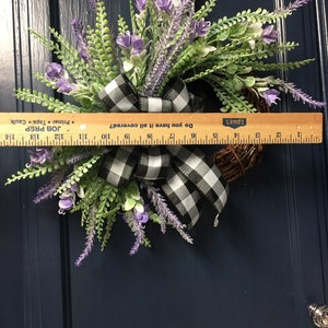 May include: A lavender and greenery wreath with a black and white checkered ribbon. The wreath is approximately 15 inches in diameter. The wreath is hanging on a blue door.