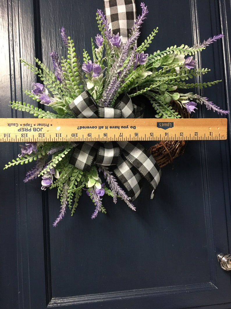 May include: A lavender and greenery wreath with a black and white checkered ribbon. The wreath is approximately 15 inches in diameter. The wreath is hanging on a blue door.