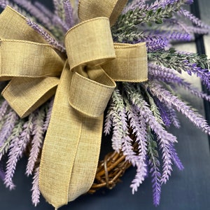 May include: A lavender wreath with a burlap bow. The wreath is made of twigs and is decorated with purple lavender sprigs.