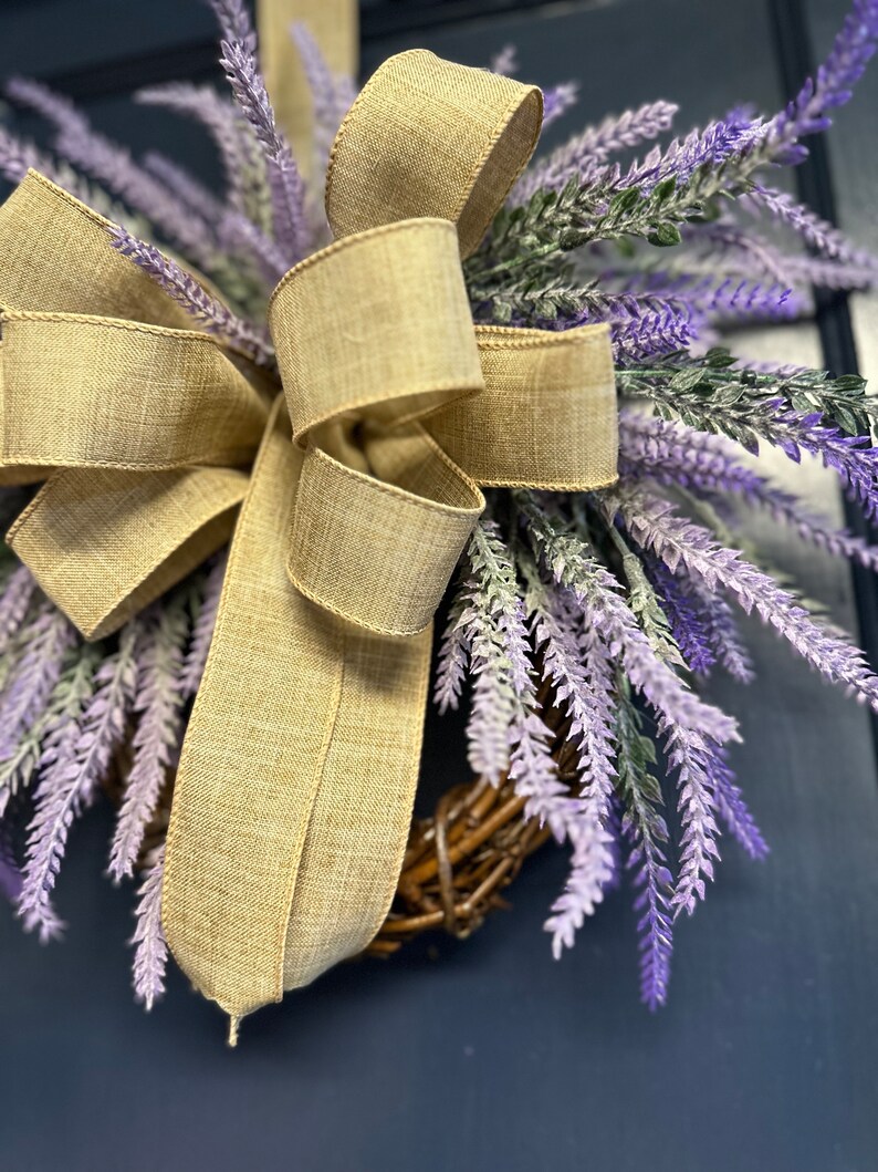 May include: A lavender wreath with a burlap bow. The wreath is made of twigs and is decorated with purple lavender sprigs.