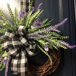 May include: A wreath made of brown twigs with a black and white checkered ribbon bow and purple lavender flowers.