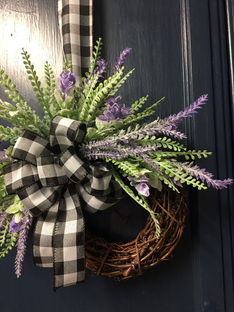 May include: A wreath made of brown twigs with a black and white checkered ribbon bow and purple lavender flowers.