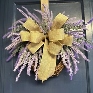 May include: A lavender wreath with a large burlap bow. The wreath is hanging on a dark blue door.