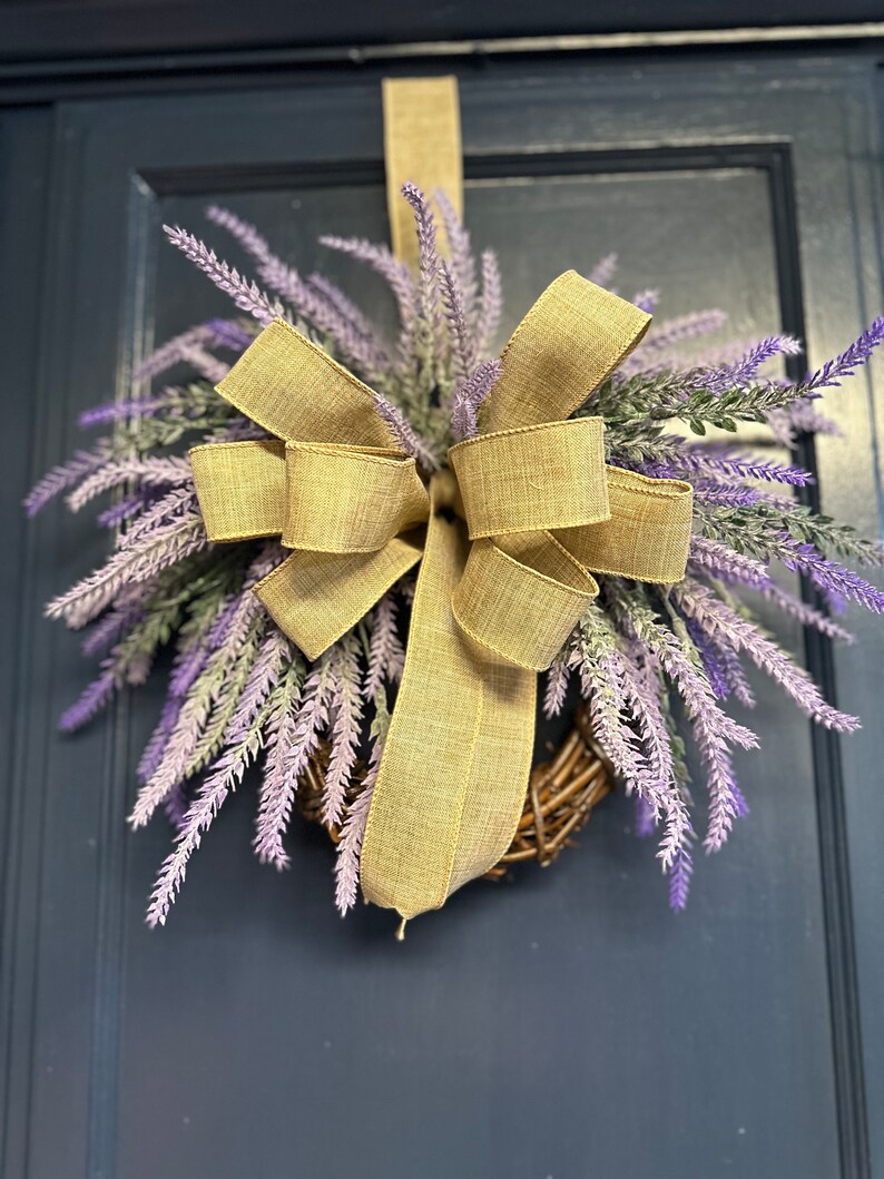 May include: A lavender wreath with a large burlap bow. The wreath is hanging on a dark blue door.