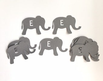 May include: Gray paper cutouts of elephants with the letter "E" cut out of the center of each elephant. There are 7 elephants in total.