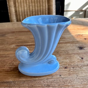 May include: A light blue ceramic vase with a trumpet shape and a curled base.