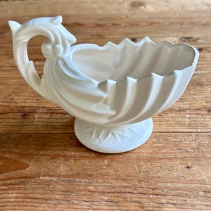May include: White ceramic planter with a fluted design and a handle shaped like a bird's head.