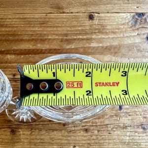 May include: A clear glass goblet with a cut crystal design is measured with a yellow tape measure that reads "25 ft" and "STANLEY".