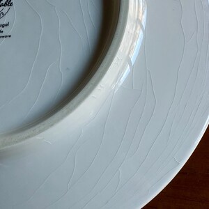Peut inclure: Gros plan sur une assiette en c&eacute;ramique blanche avec un motif craquel&eacute;. L'assiette a un bord l&eacute;g&egrave;rement sur&eacute;lev&eacute; et une surface lisse et brillante. L'assiette est marqu&eacute;e "Table" et "Portugal".