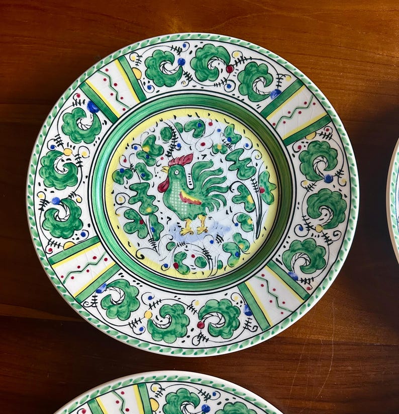 Peut inclure: Assiette en c&eacute;ramique peinte &agrave; la main avec un motif de coq. L'assiette pr&eacute;sente une bordure verte avec des accents blancs et jaunes. Le centre de l'assiette pr&eacute;sente une illustration de coq avec des d&eacute;tails verts et rouges. L'assiette mesure environ 25 cm de diam&egrave;tre.