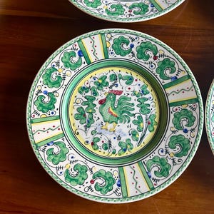 Peut inclure: Ensemble d'assiettes d&eacute;coratives en c&eacute;ramique avec un motif de coq. Les assiettes pr&eacute;sentent une palette de couleurs verte, jaune et blanche avec des motifs floraux et g&eacute;om&eacute;triques complexes. Le coq est au centre de l'assiette.