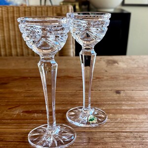 May include: Two clear crystal stemmed glasses with a cut design. The glasses are on a wooden table.