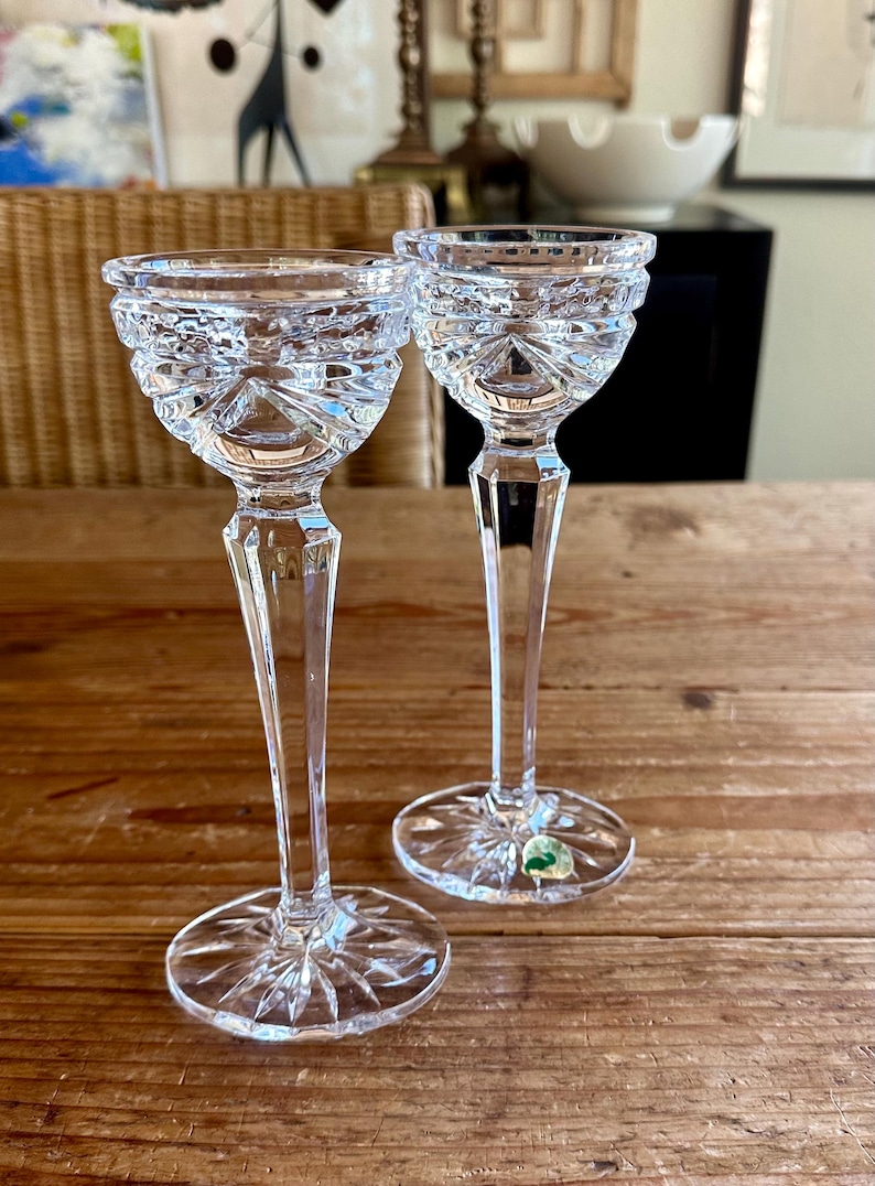 May include: Two clear crystal stemmed glasses with a cut design. The glasses are on a wooden table.