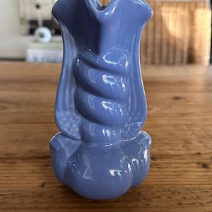 May include: A small, light blue ceramic vase with a twisted design and a rounded base. The vase is shaped like a flower.