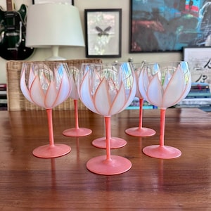May include: A set of six wine glasses with a tulip design. The glasses have a clear bowl with a white and peach-colored tulip design. The stems and bases are peach-colored.