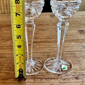 May include: Two clear glass candle holders with a cut glass design. The candle holders are approximately 7 inches tall and are measured against a yellow tape measure.