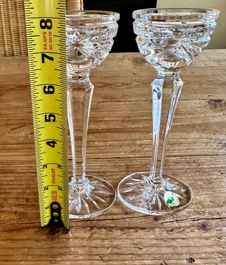 May include: Two clear glass candle holders with a cut glass design. The candle holders are approximately 7 inches tall and are measured against a yellow tape measure.