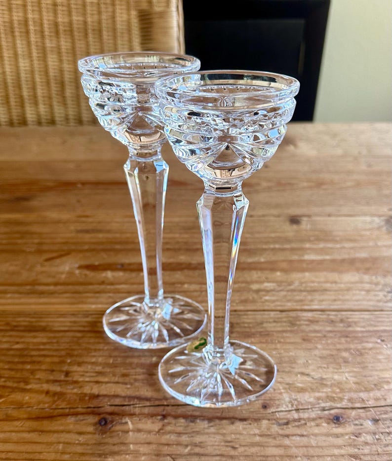 May include: Two clear glass candle holders with a cut glass design. The candle holders have a tall, slender stem and a wide, round base.