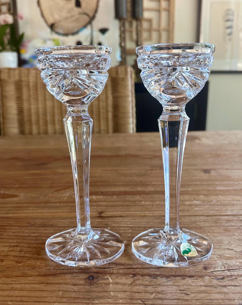May include: Two clear glass candle holders with a cut crystal design. The candle holders have a tall, slender stem and a wide base.
