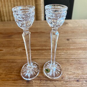 May include: Two clear glass candle holders with a cut crystal design. The candle holders have a tall, slender stem and a round base.