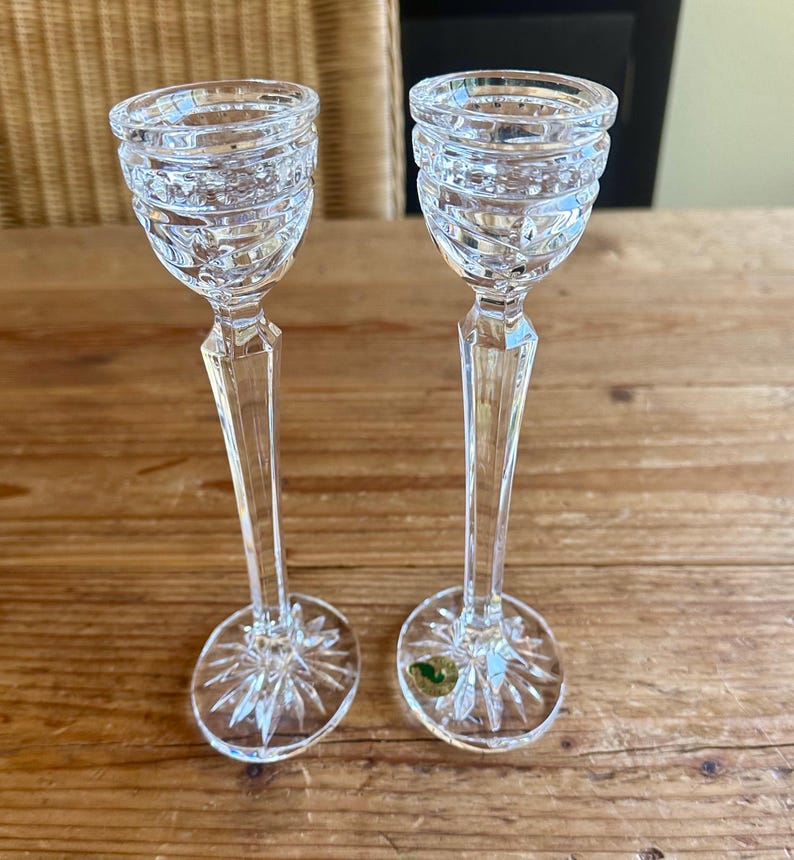 May include: Two clear glass candle holders with a cut crystal design. The candle holders have a tall, slender stem and a round base.