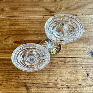 May include: Two clear glass candle holders with a decorative, circular, cut-glass design. The candle holders are on a wooden surface.