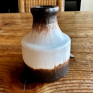 May include: A brown and white ceramic vase with a glazed finish. The vase has a rounded body and a narrow neck.