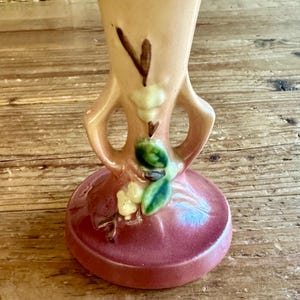 May include: A vintage ceramic vase with a pink and brown glaze. The vase has two handles and a floral design with white flowers and green leaves.