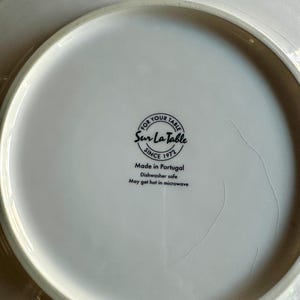 Peut inclure: Assiette en c&eacute;ramique blanche avec le texte "FOR YOUR TABLE Sur La Table SINCE 1972 Made in Portugal Dishwasher safe May get hot in microwave". L'assiette est de forme circulaire.