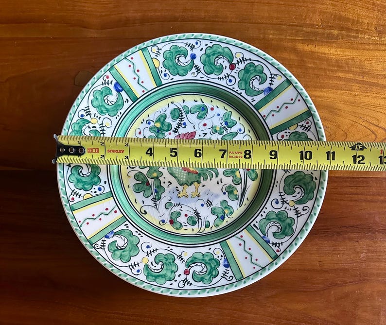 Peut inclure: Une assiette d&eacute;corative en c&eacute;ramique avec un motif de coq. L'assiette pr&eacute;sente une bordure verte et blanche avec un centre jaune. L'assiette mesure environ 30 cm de diam&egrave;tre.