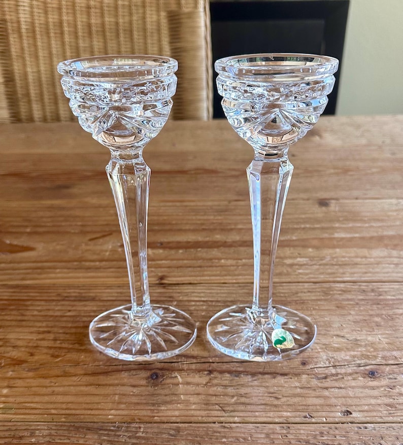 May include: A pair of clear glass candle holders with a cut glass design. The candle holders have a tall, slender stem and a round base.