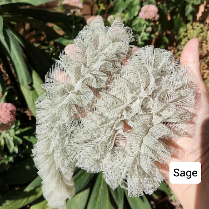 Pu&ograve; includere: Una passamaneria in tulle arricciato color verde salvia caratterizzata da una delicata trama a rete trasparente con strati raccolti. Il tessuto &egrave; disposto in una striscia ondulata continua di una tonalit&agrave; verde tenue con un'etichetta con il testo Sage.