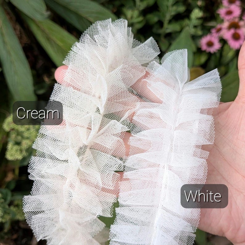 Pu&ograve; includere: Due strisce di nastro in tulle arricciato, una color crema tenue e una color bianco brillante. Ogni striscia presenta una trama a rete increspata e stratificata con un motivo a griglia fine e semitrasparente. Testo Cream e White visibile.