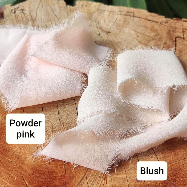 Puede incluir: Dos tiras de cinta de tela suave de color claro con bordes deshilachados y sin rematar. Una cinta est&aacute; etiquetada como Powder pink y la otra como Blush. Las cintas est&aacute;n dispuestas en pliegues sueltos y fluidos, mostrando una textura mate.