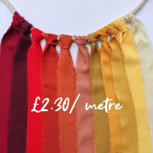 Peut inclure: Une guirlande décorative composée de bandes de tissu verticales dans un dégradé de couleurs allant du bordeaux profond et rouge à l'orange, pêche, jaune moutarde et crème. Chaque bande est nouée sur une cordelette blanche torsadée.
