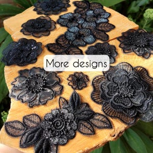 May include: A collection of black floral lace appliques featuring intricate embroidery, shimmering thread details, and layered petals. The pieces vary in size and shape, showcasing diverse botanical patterns with a text overlay reading More designs.